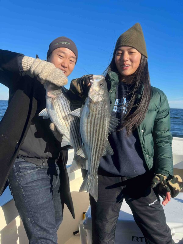 Two people holding a striped fish on the water.