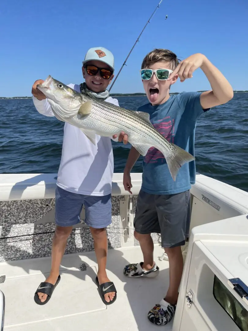 Two men holding a striped bass on the boat.